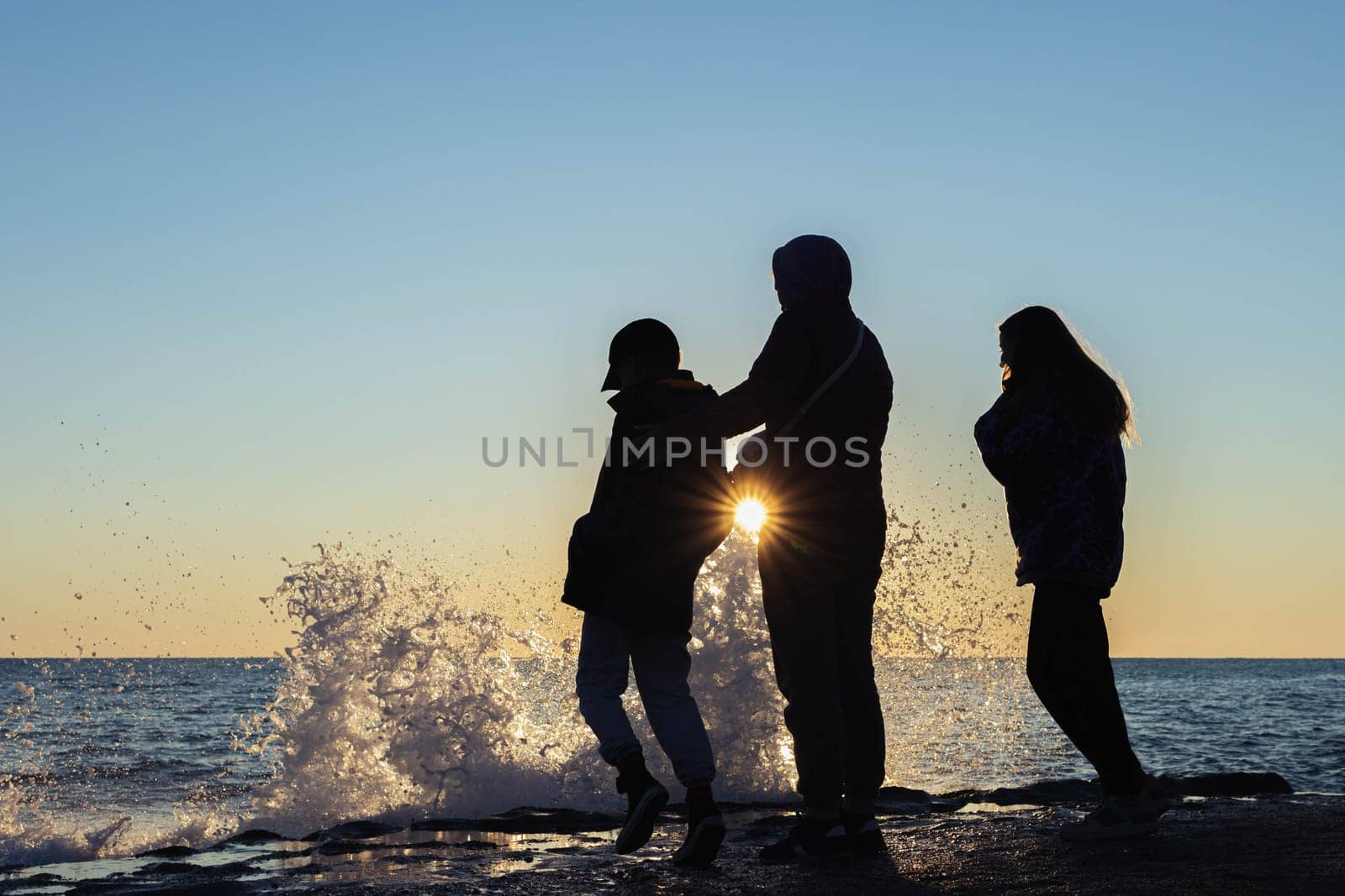 on the seashore, a family of mother, daughter and son look at the waves, there is a place for an inscription people stand with their backs at sunset. High quality photo