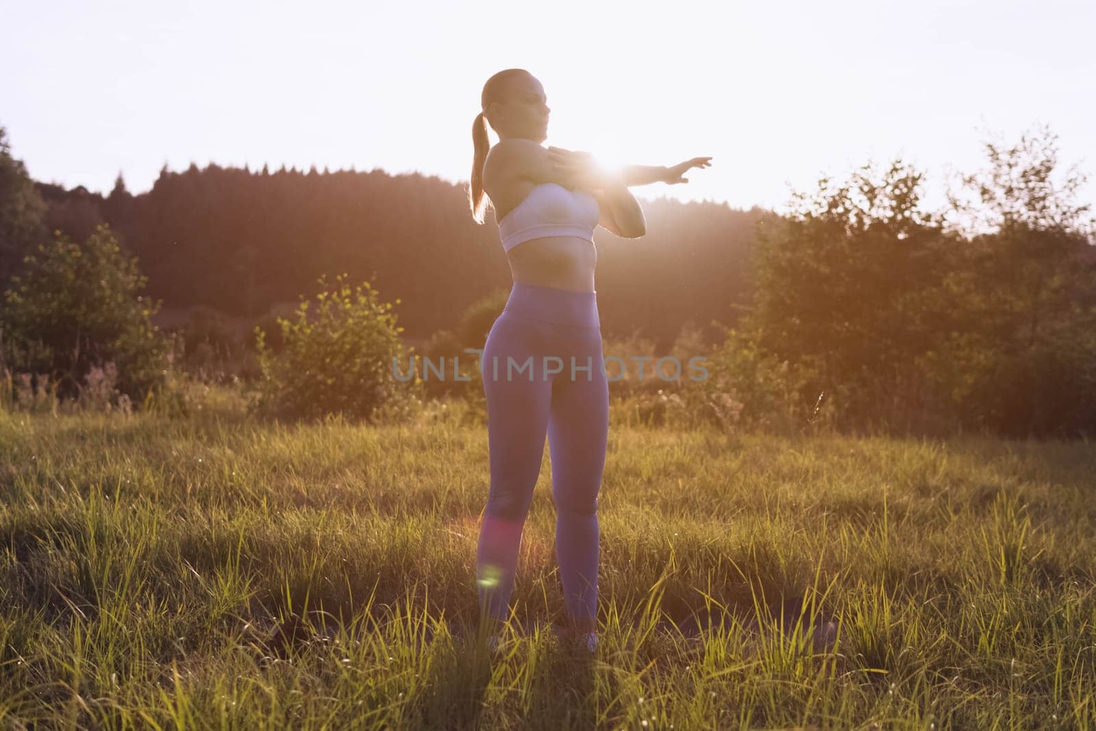 a girl of fair appearance with tied hair, in a fitness suit, is engaged in exercises at dawn in the by PopOff