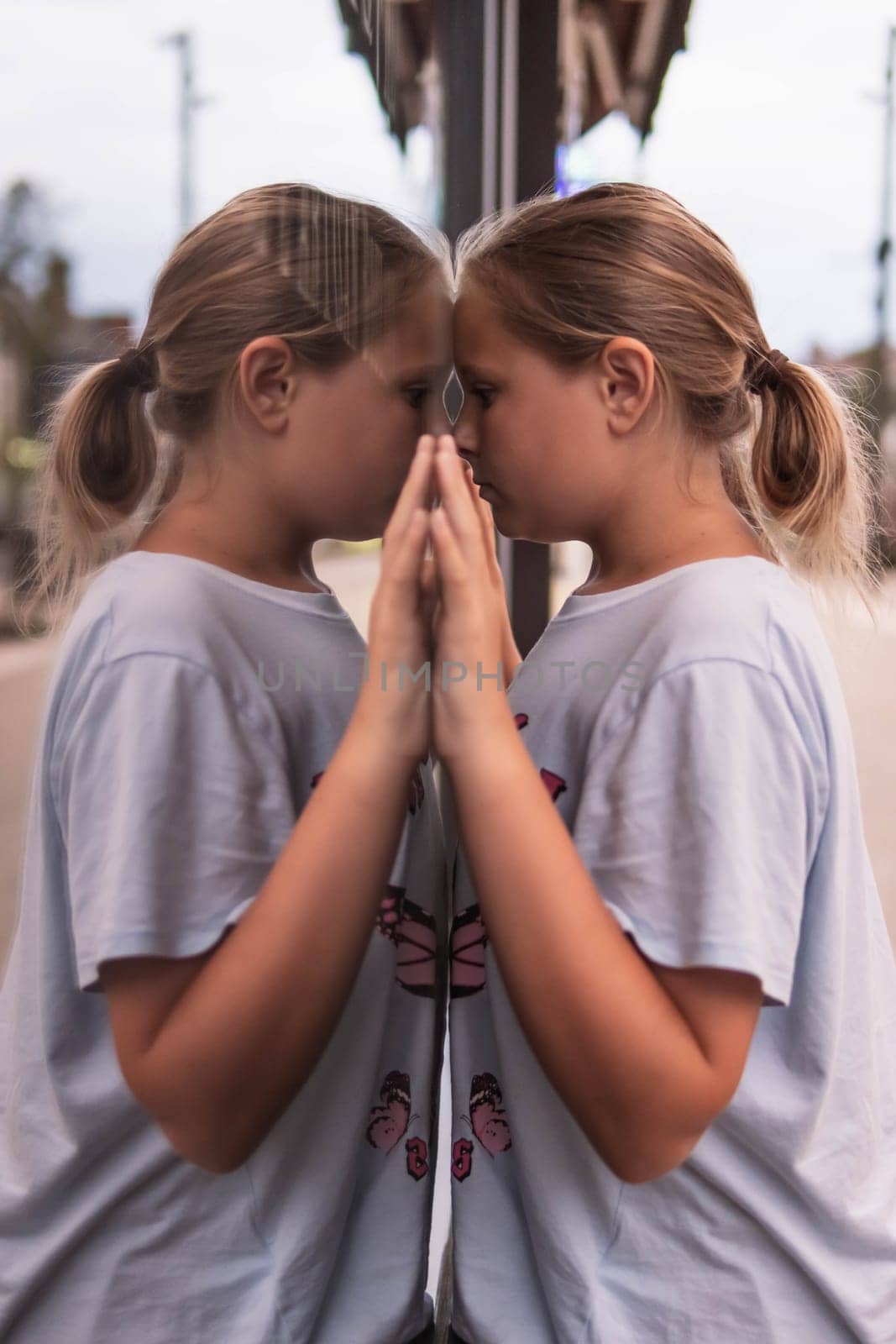 A teenager of European appearance with blond hair braided in a ponytail stands near a glass showcase and looks into it, a reflection of a girl is on the glass showcase. High quality photo