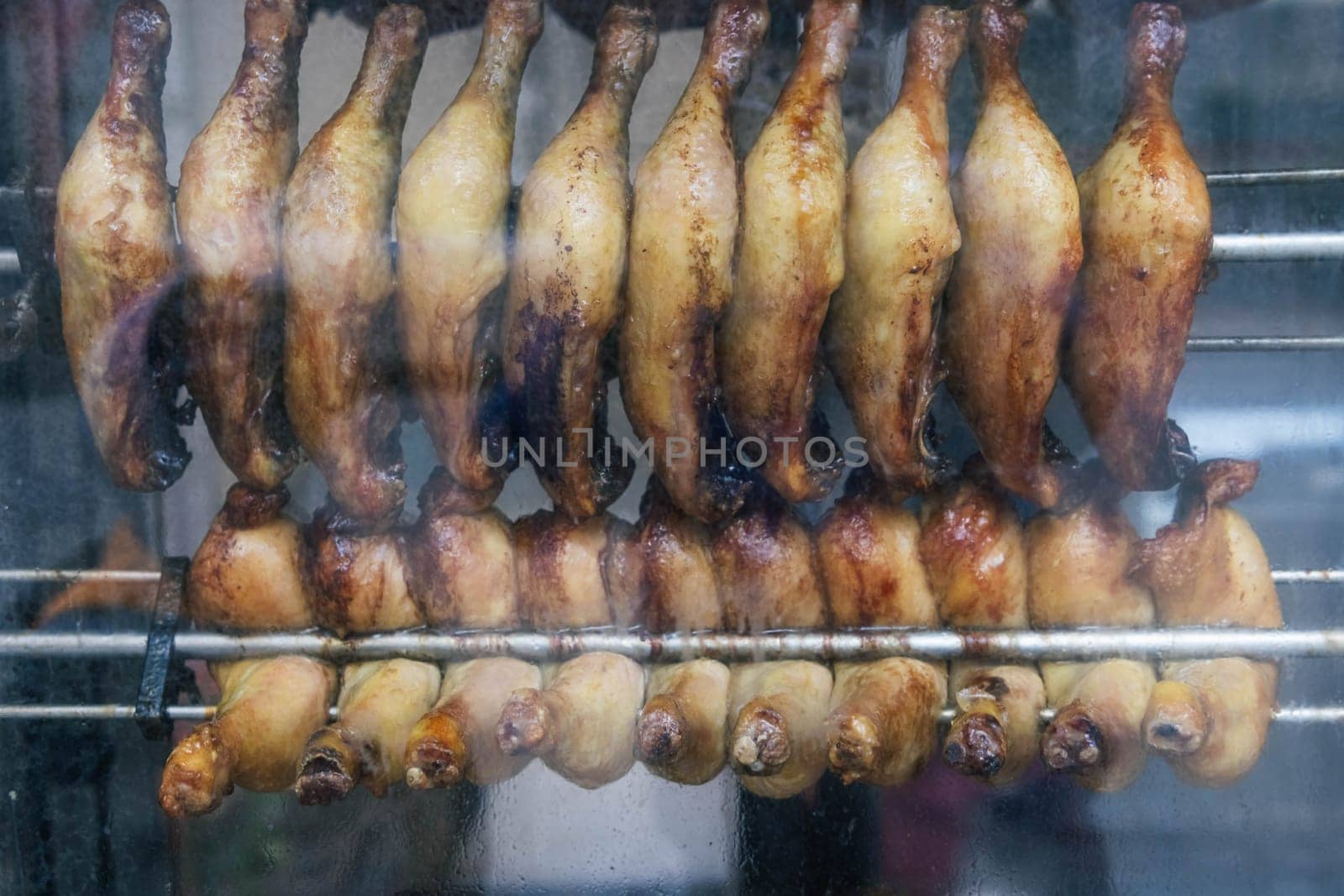 chicken legs are fried in a shop window for sale to hungry people, smoke a grill. High quality photo