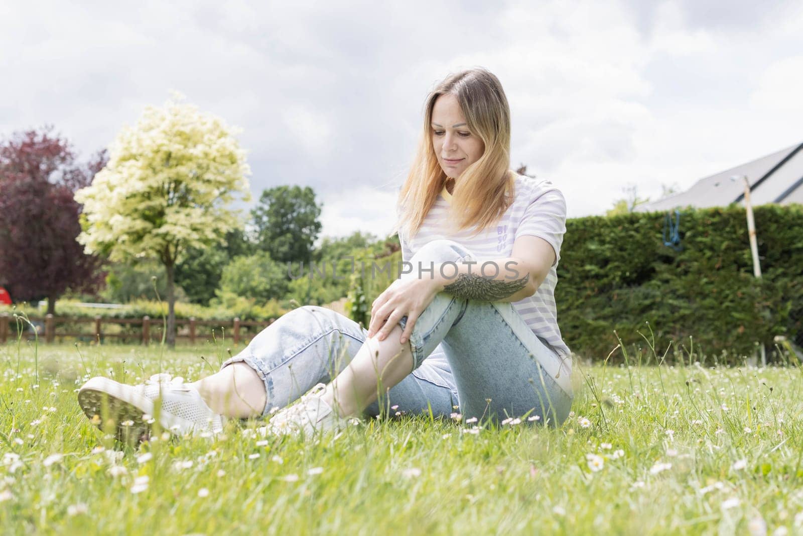 a girl with blond hair of European appearance sits in a park on green grass by PopOff