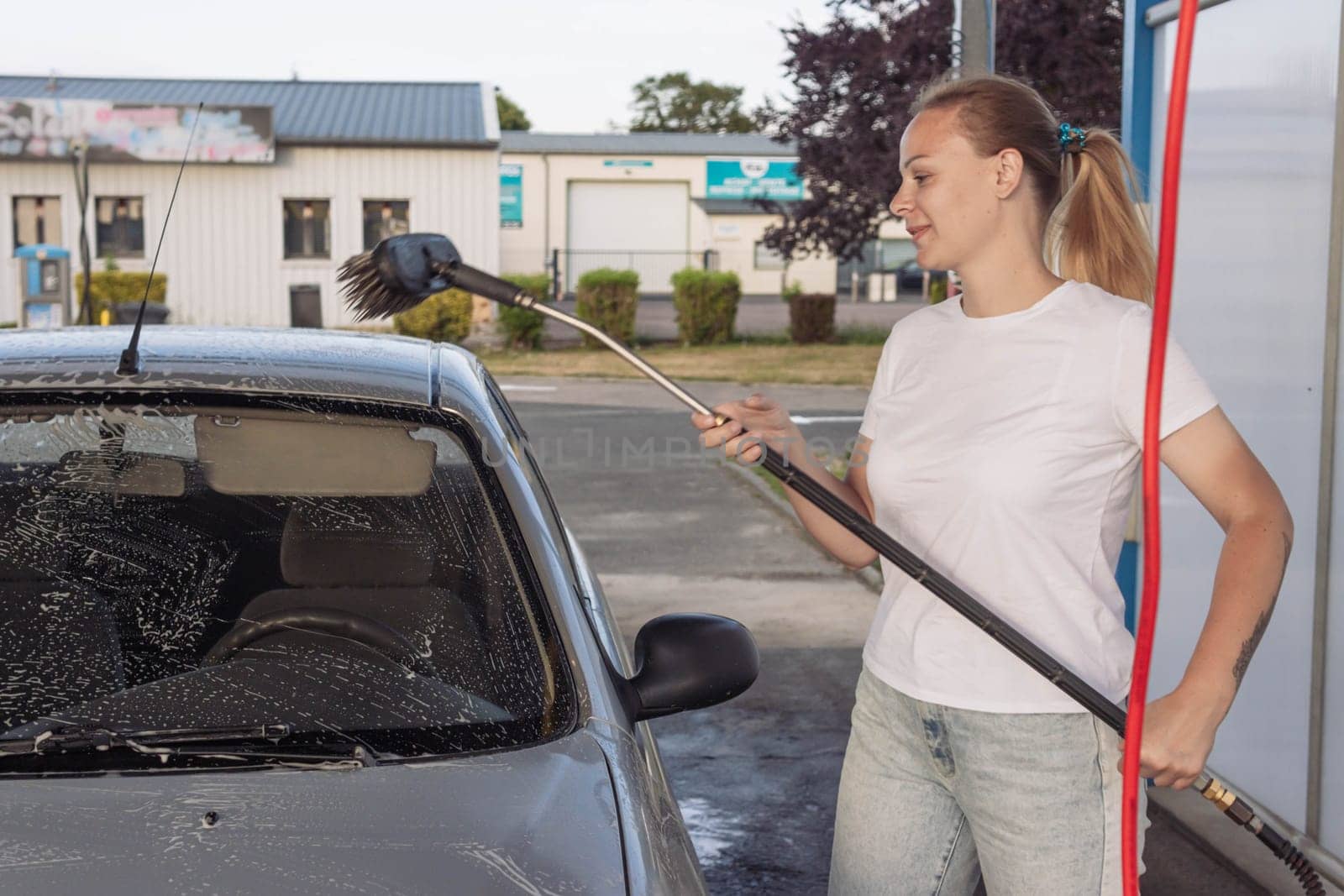 a girl with blond hair in a white T-shirt and jeans washes a car at a self-service car wash. High quality photo