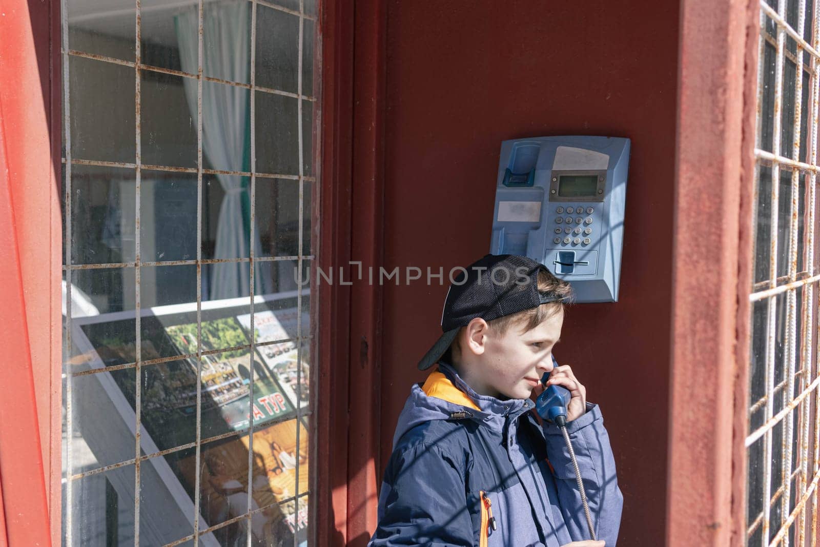 a boy of European appearance in a telephone booth is talking on the phone. Old telephone booth. Vintage and retro. High quality photo