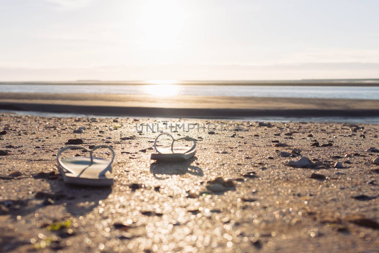 on the beach on the sand, a pair of beach slippers stands close-up and the background is blurred at sunset, the photo is taken, a beautiful and creative beach background High quality photo