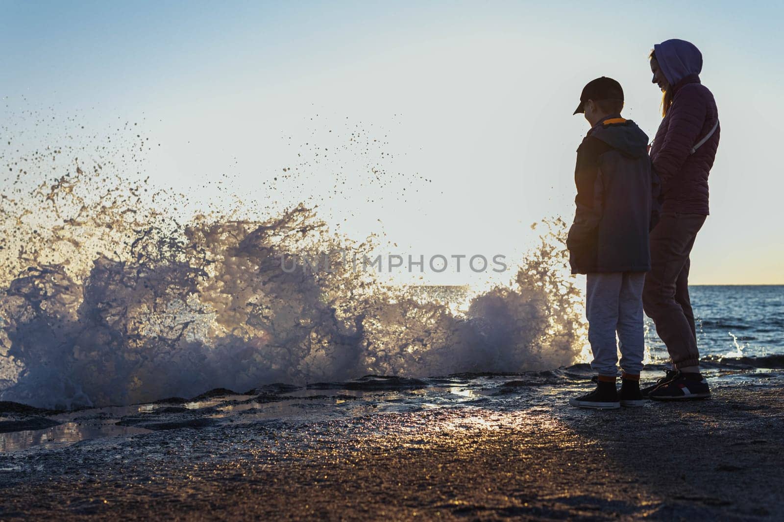 on the seashore, mom and son look at the waves, there is a place for an inscription people stand with their backs. High quality photo