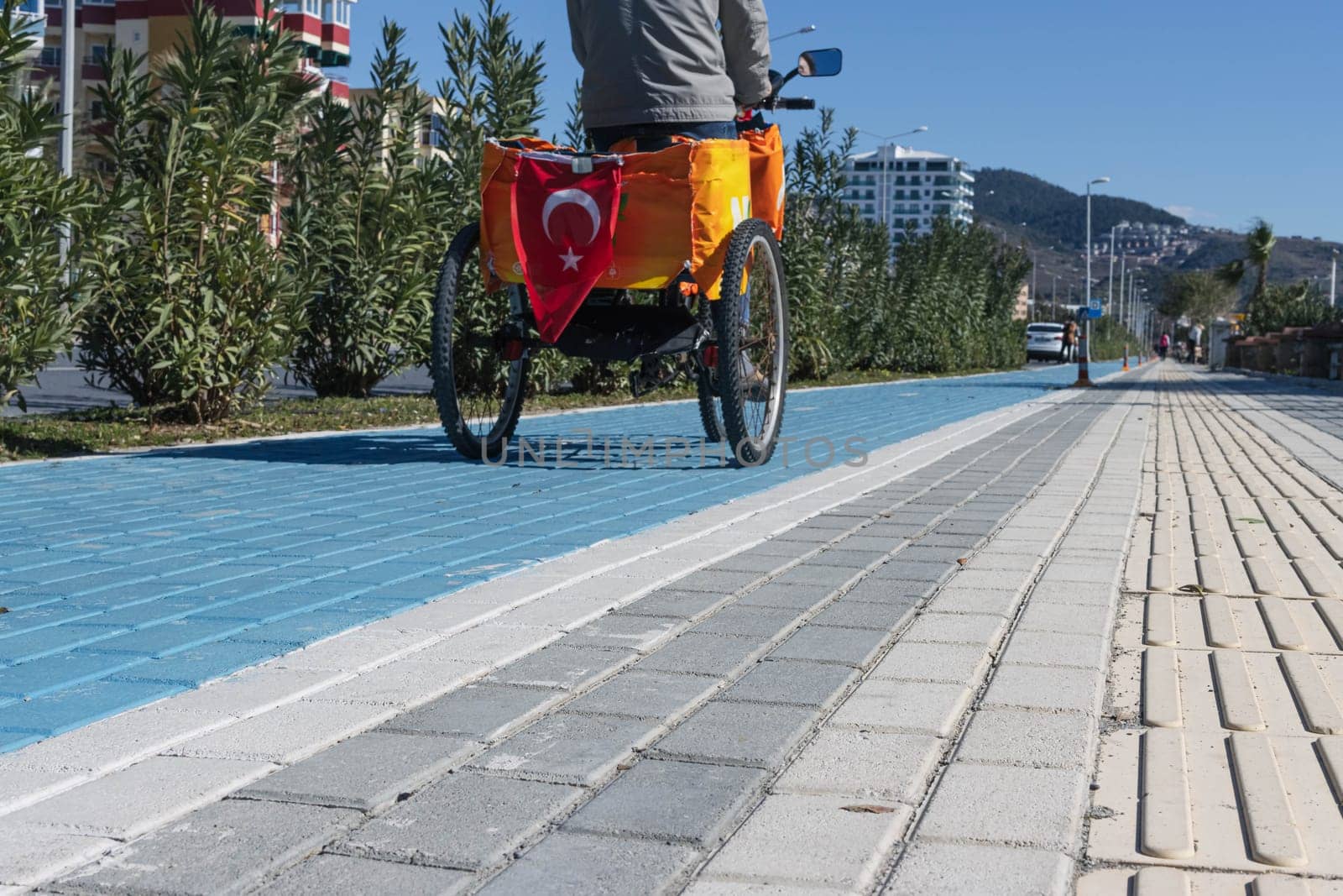 a man rides down the street on a three-wheeled bicycle along a cycle path with markings, the Turkish flag hangs on the back of the bicycle. High quality photo