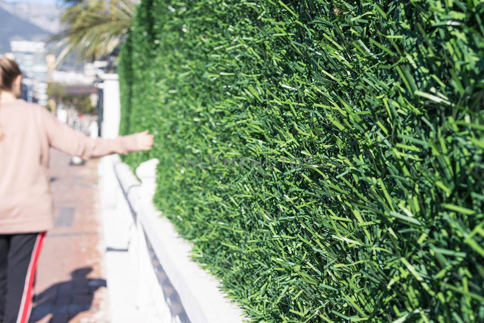 A girl walks next to a hedge and a fence close-up phot by PopOff