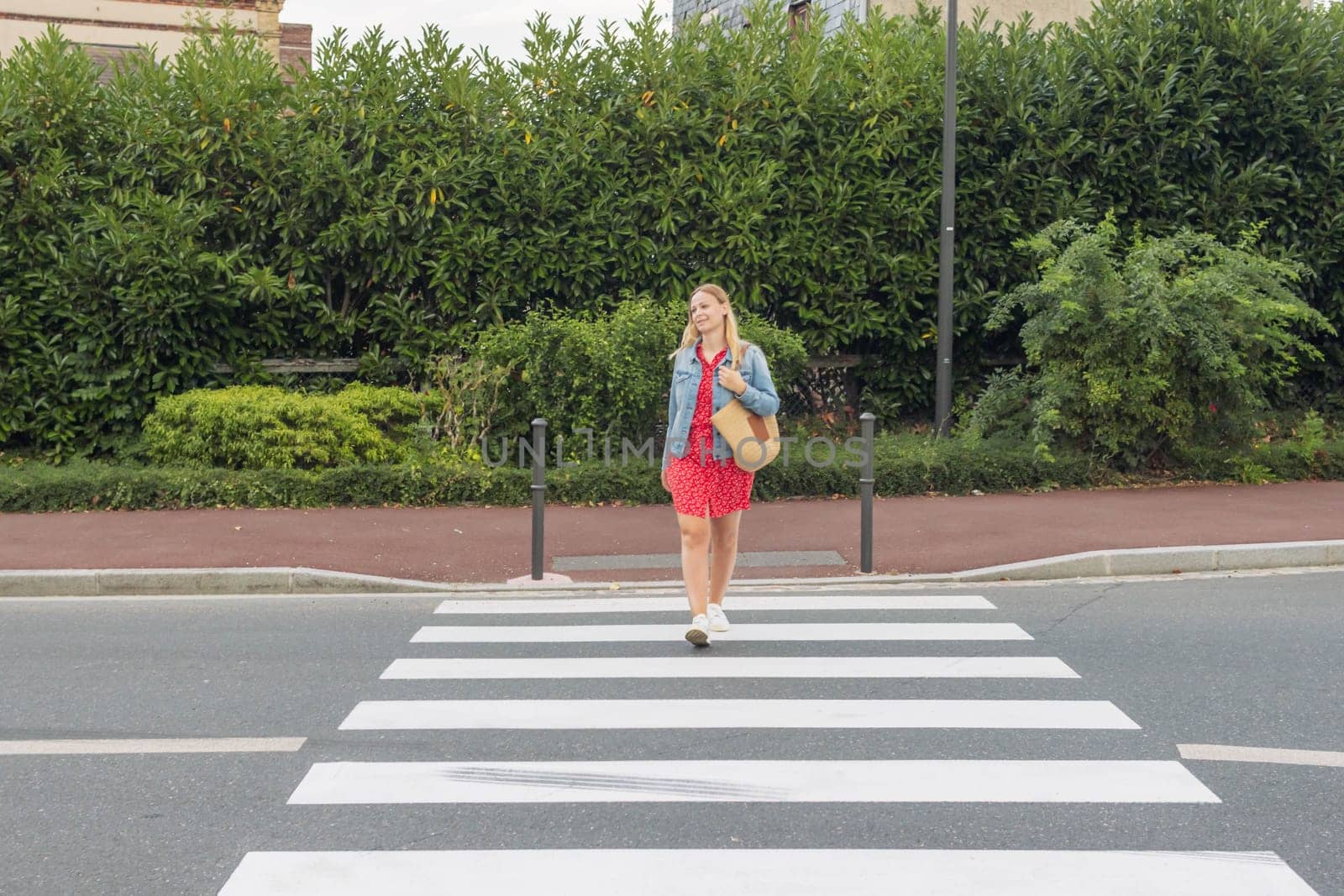 a girl in a red dress crosses the road at a pedestrian crossing beautiful woman in the city in summer. High quality photo