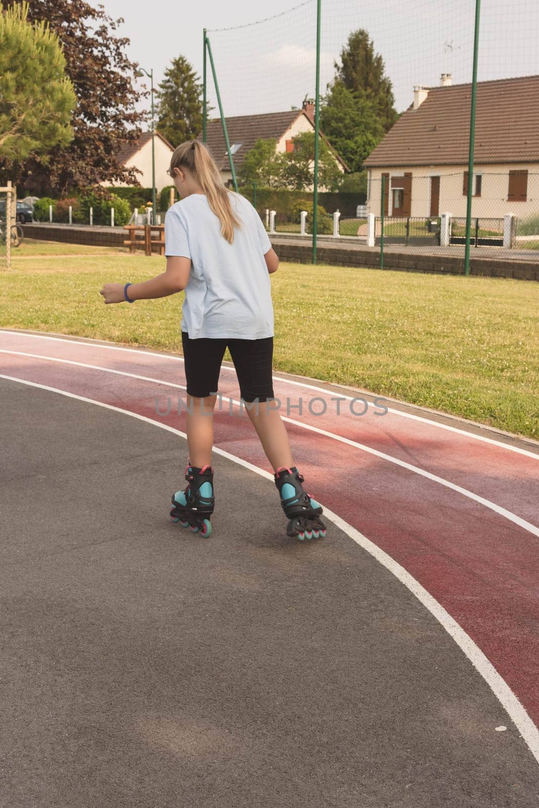 child of European appearance with blond hair tied in a ponytail learn to roller skate in the park dressed girl in a light T-shirt and black shorts. High quality photo
