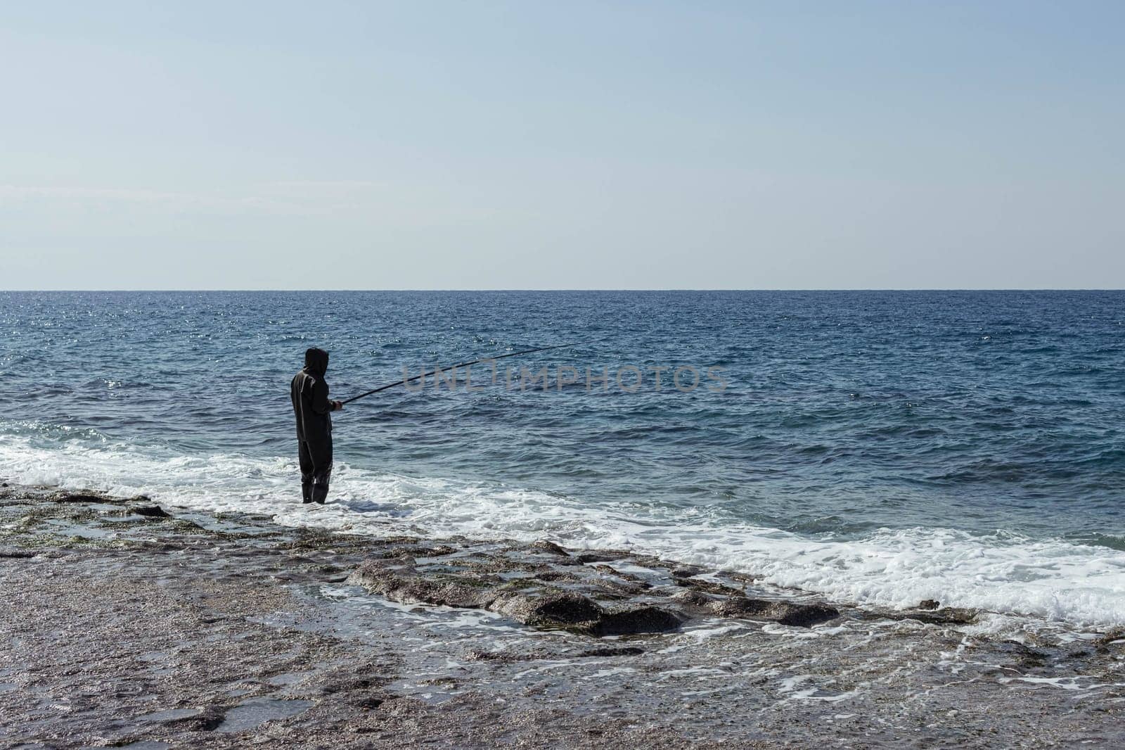 a man fishes in the sea or river in a rubber suit with a fishing rod in his hands. High quality photo