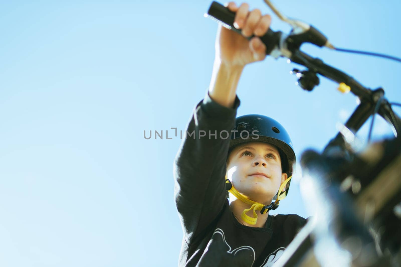 portrait of a teenager boy against the blue sky, a child on a bicycle in a black helmet to protect his head. there is a place for an inscription. High quality photo