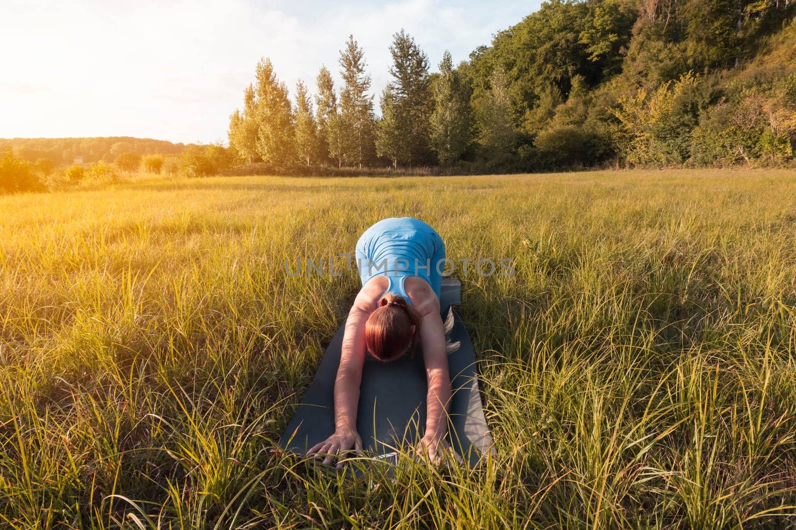 girl of fair appearance with tied hair,dressed in blue clothes for phineas,does yoga outdoors at sunset.healthy lifestyle concept,there is a place for an inscription. High quality photo