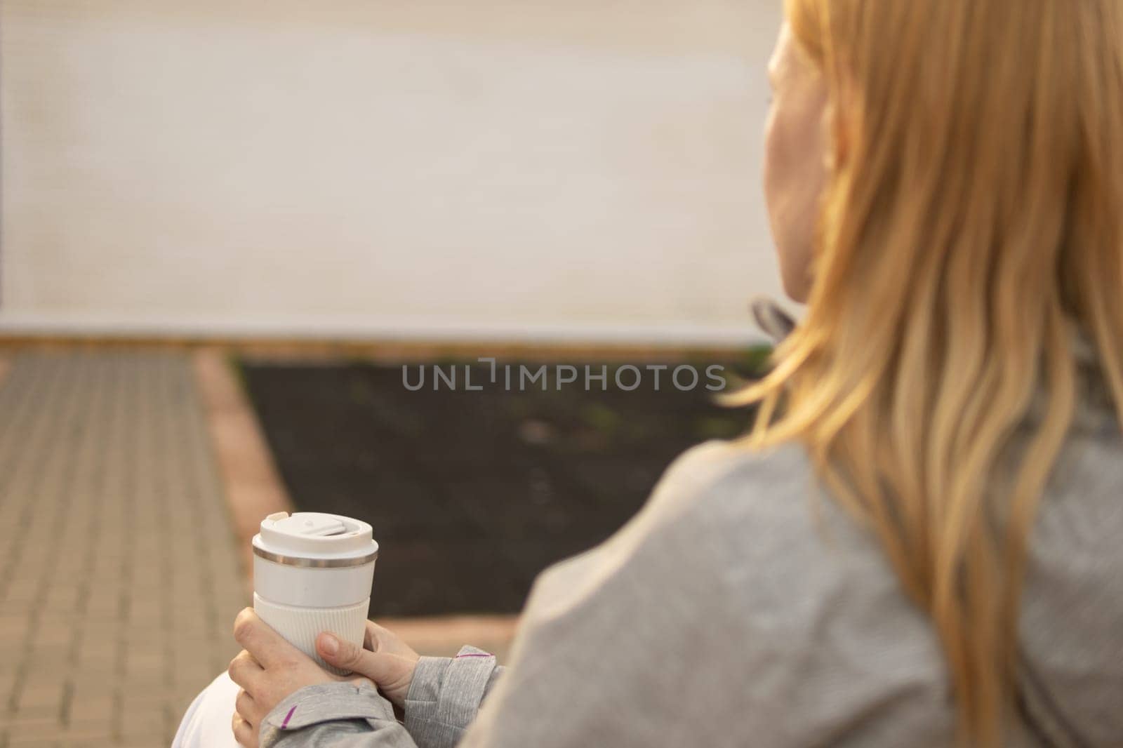 back photo of a girl who is sitting on a bench in the park holding a white thermo mug for tea by PopOff