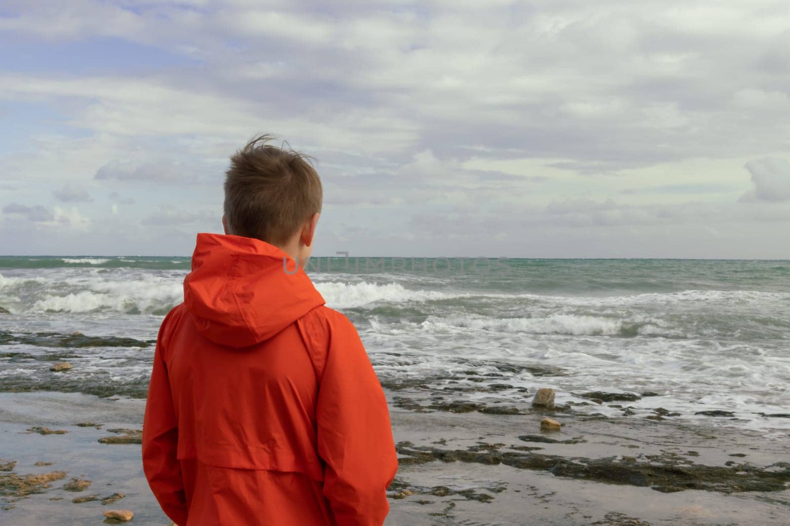 a boy with blond hair in an orange windbreaker, stands with his back on the embankment close-up, there is a place for an inscription. High quality photo