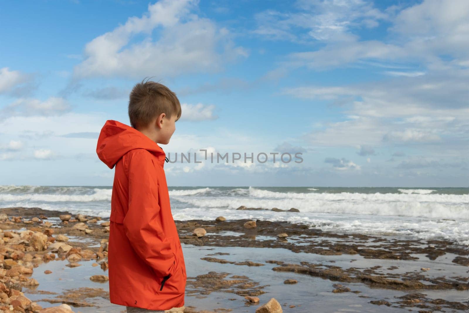 a boy with blond hair in an orange windbreaker, stands with his back on the embankment close-up, there is a place for an inscription. High quality photo