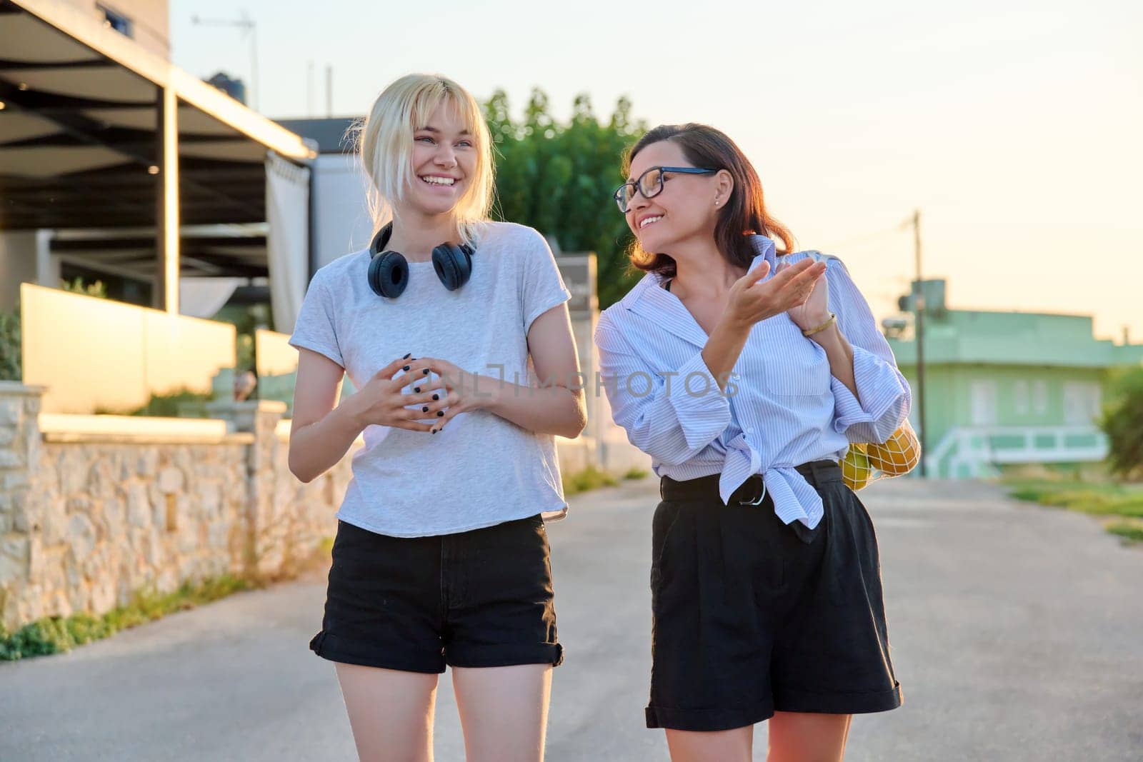 Outdoor portrait of happy mom and teenage daughter walking together in summer in sunset light. Family, communication, motherhood, mother's day, adolescence concept