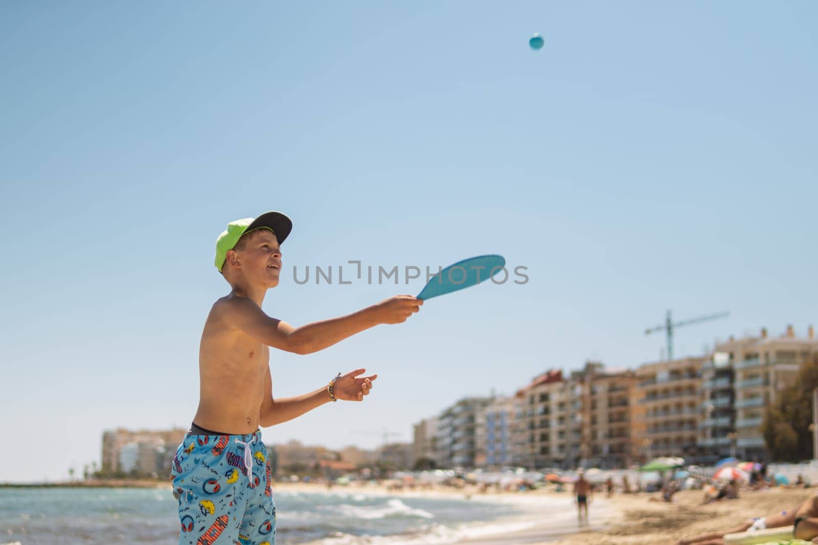 a child of European appearance in the summer on the beach walks in tennis, the boy is standing in bathing shorts and in a green cap on the beach, a happy child is resting on the sea.High quality photo