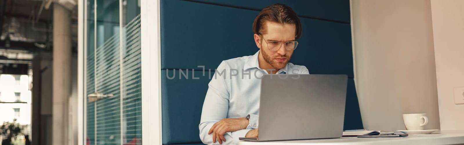Busy male manager drinking coffee during working on laptop in modern office . High quality photo