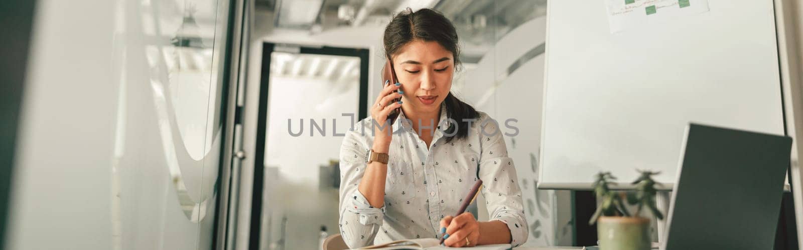 Businesswoman talking phone with client and making notes while sitting in office. High quality photo