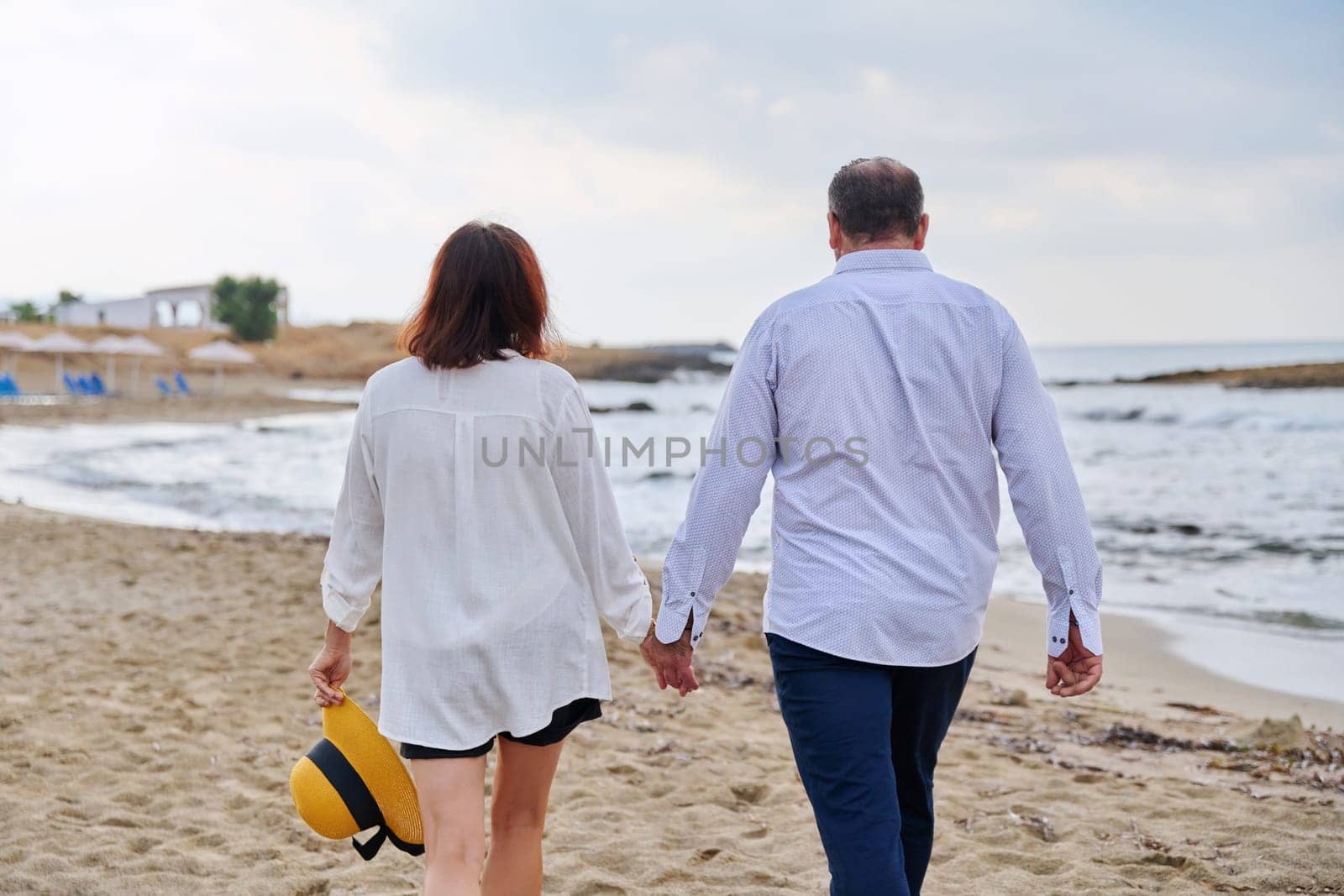 Happy middle aged couple walking together on the beach, back view by VH-studio