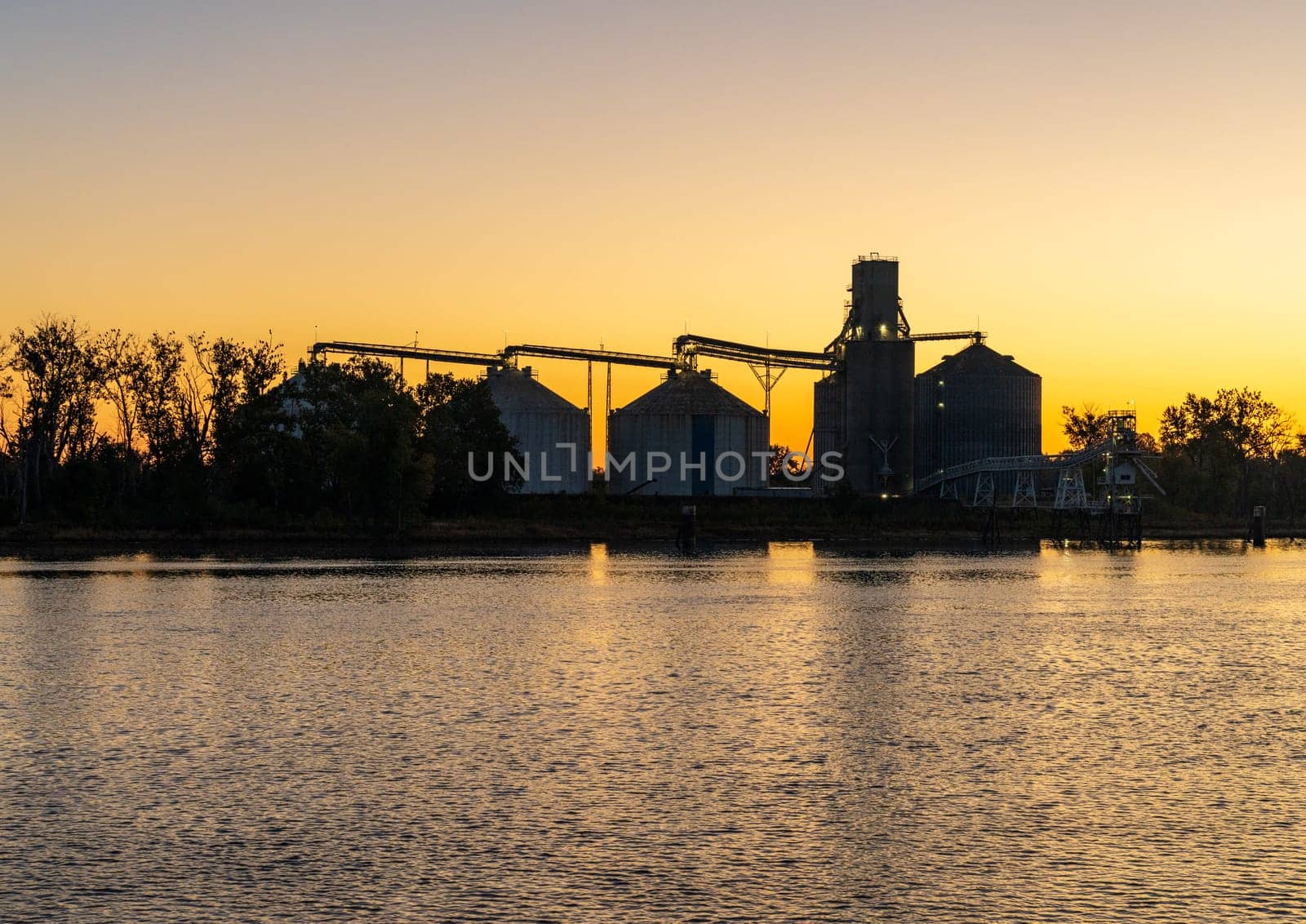 Sunrise behind large grain storage bins by Mississippi River by steheap