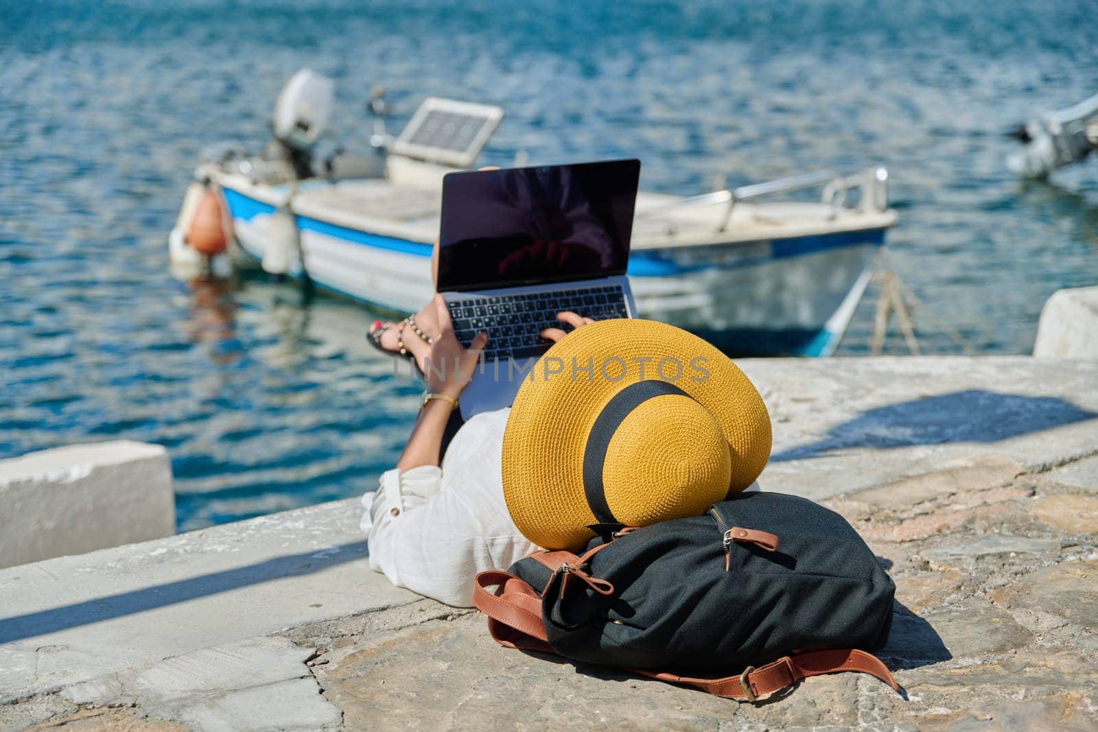 Woman in hat typing on laptop, water bay boat background by VH-studio