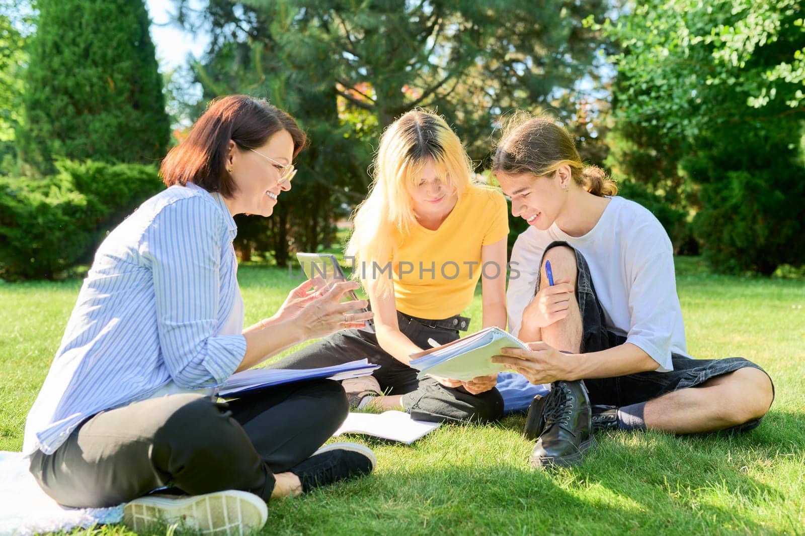 School teacher, psychologist, social worker talking to teenagers, sitting on grass by VH-studio