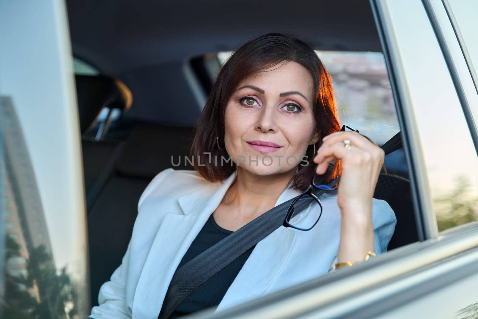 Portrait of business elegant middle-aged woman in car in back passenger seat. Beautiful confident smiling woman 45 years old looking at camera. Business, auto travel, lifestyle, people, mature age