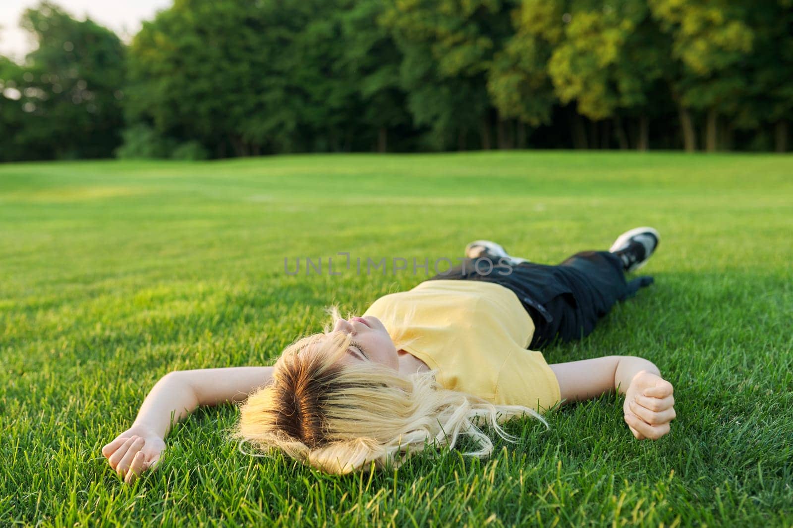 Young blonde woman lying on the grass in a summer park. by VH-studio