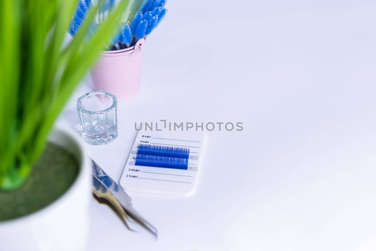 Materials for eyelash extensions.two tweezers,artificial blue eyelashes on a white background. in the background is a pink bucket with brushes for eye. On the side there is a place for an inscription