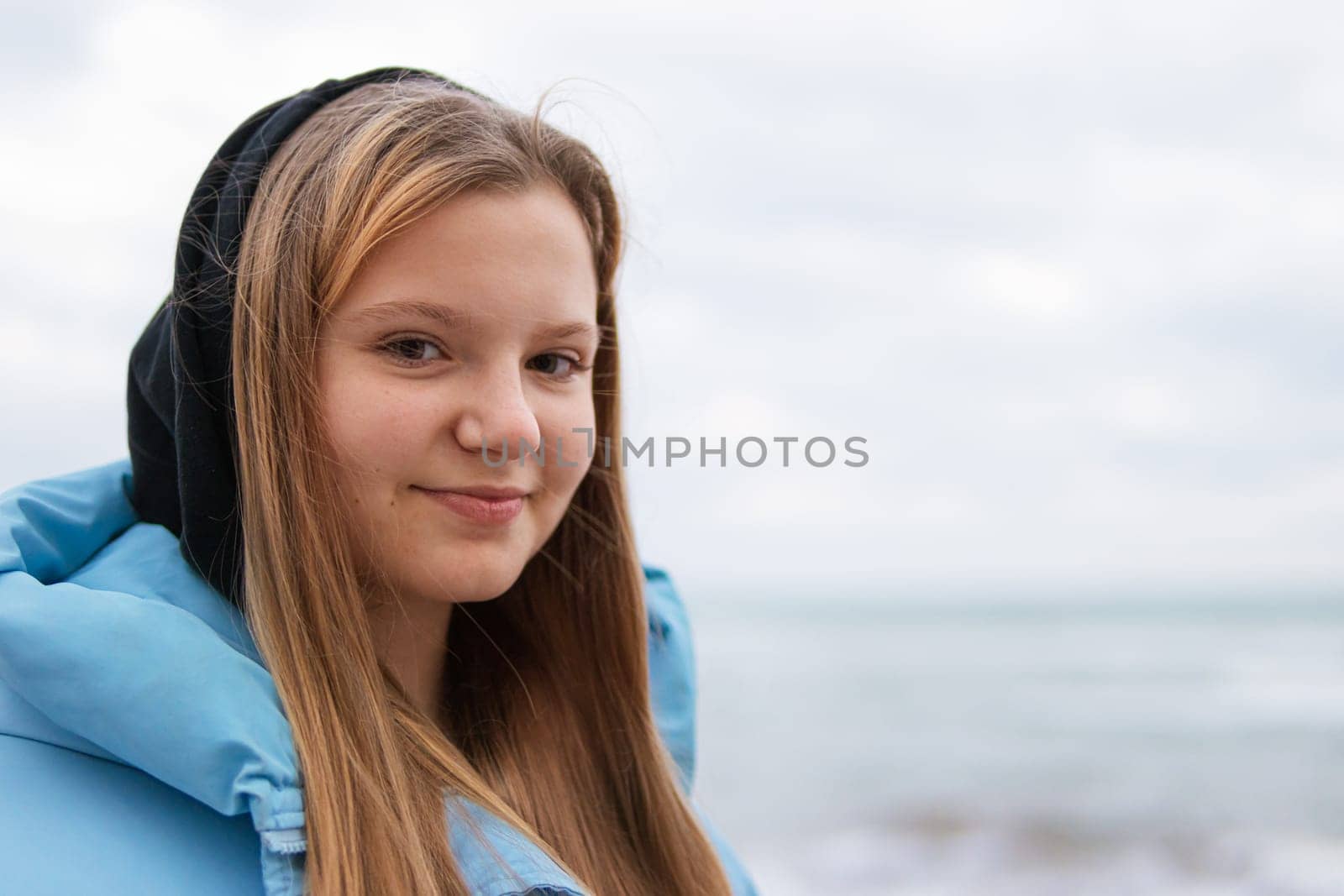 portrait of a cute girl with blond hair in a blue jacket with a hood on her head, there is a place for an inscription. High quality photo