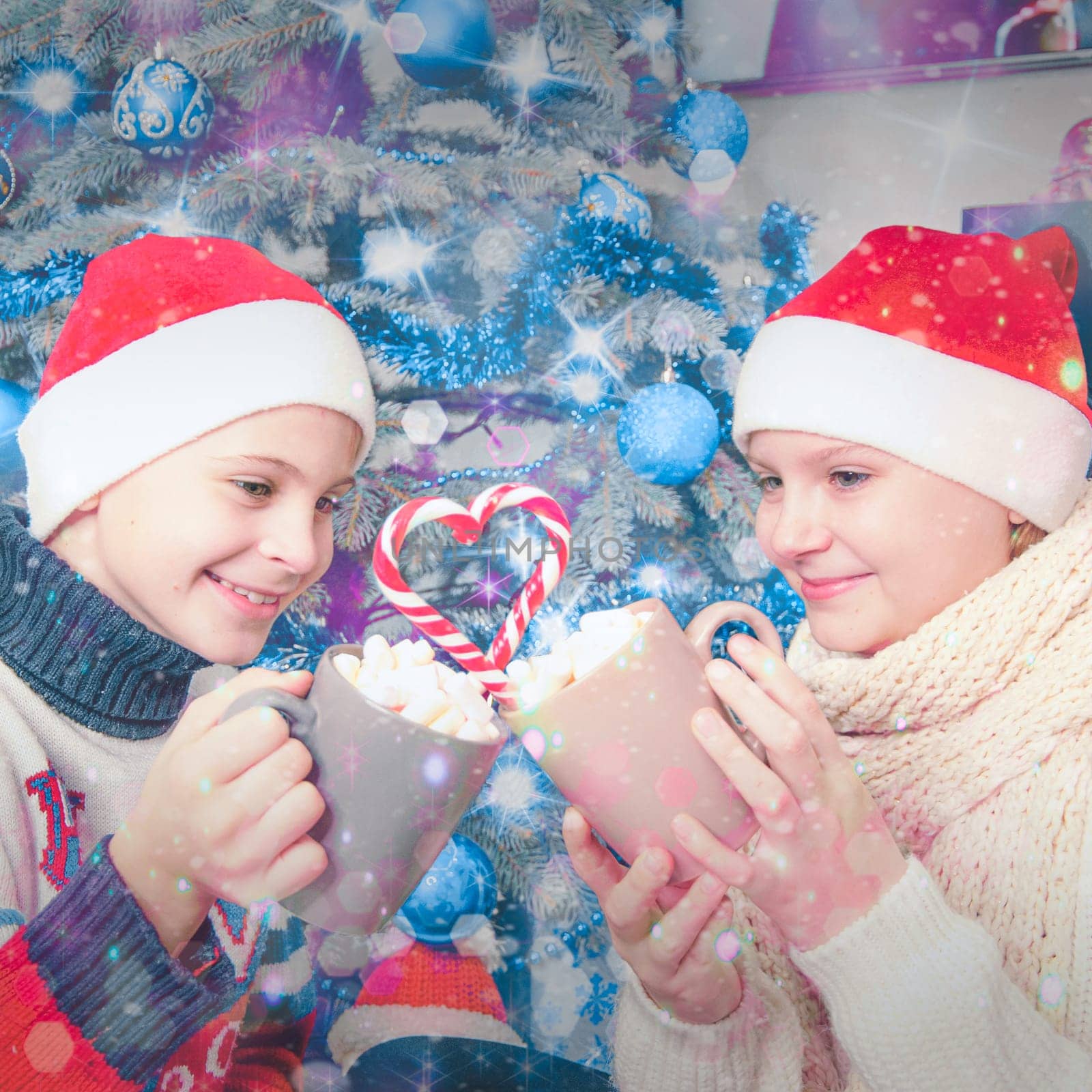 Christmas photo of children, a cheerful boy and girls in Christmas clothes are sitting near the Christmas tree, holding cups with cocoa and marshmallows in their hands. New Year. High quality photo