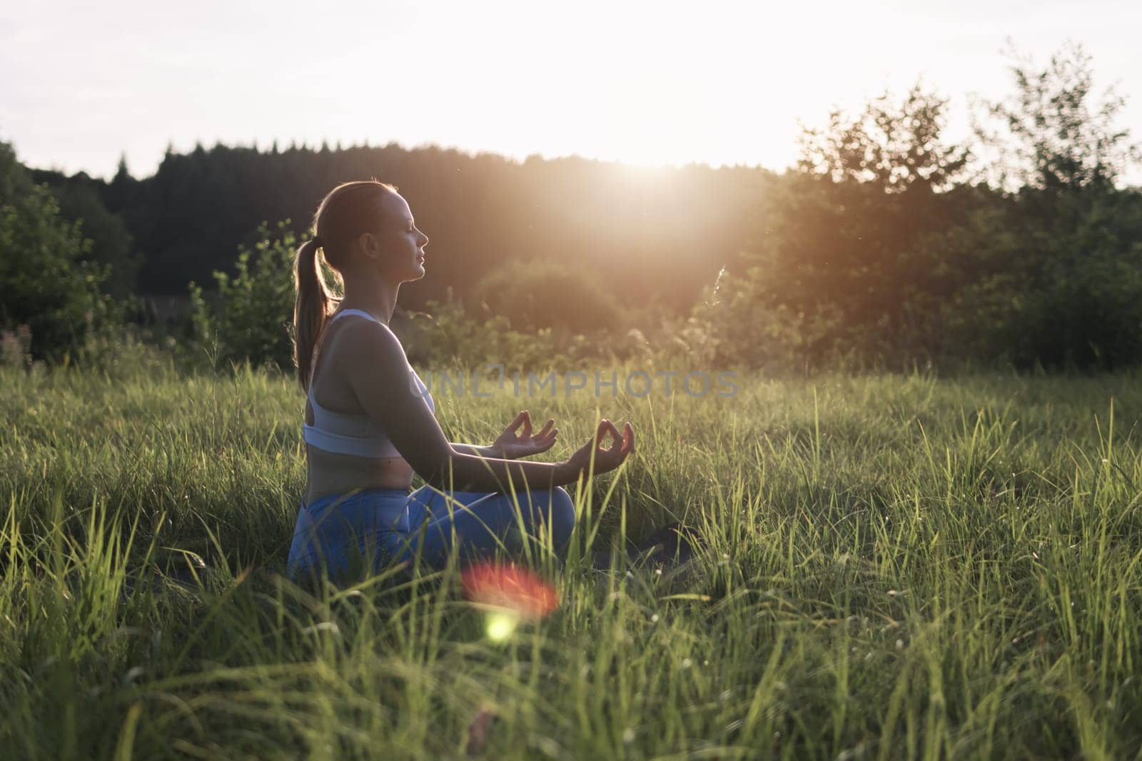 a girl of light appearance at sunset in a park doing exercises in sportswear, sitting on the grass, a silhouette of a woman, there is a place for an inscription. High quality photo