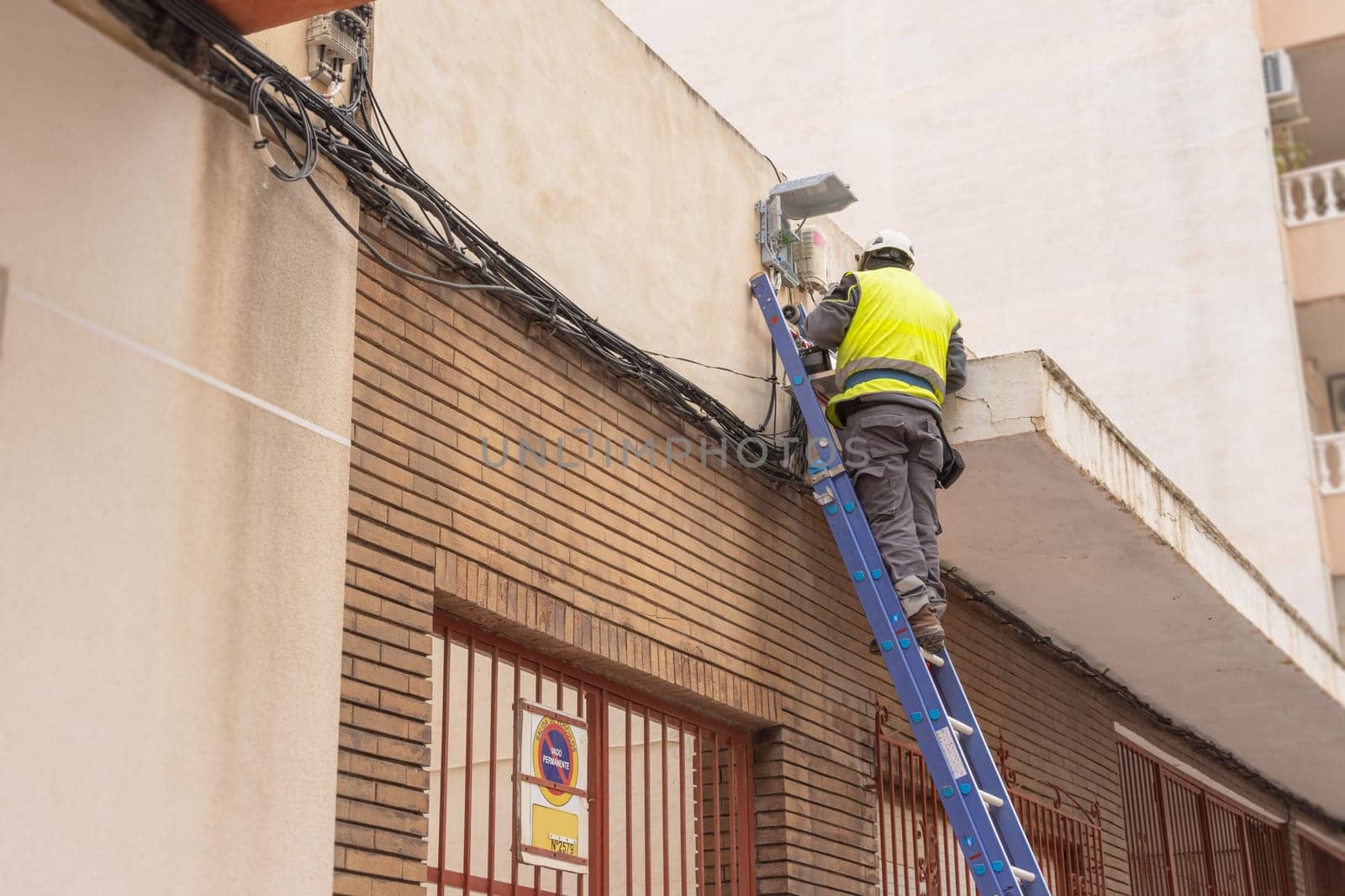 A man in a reflective vest stands on a stepladder doing electrics. A man in work clothes repairs the cable at home. High quality photo