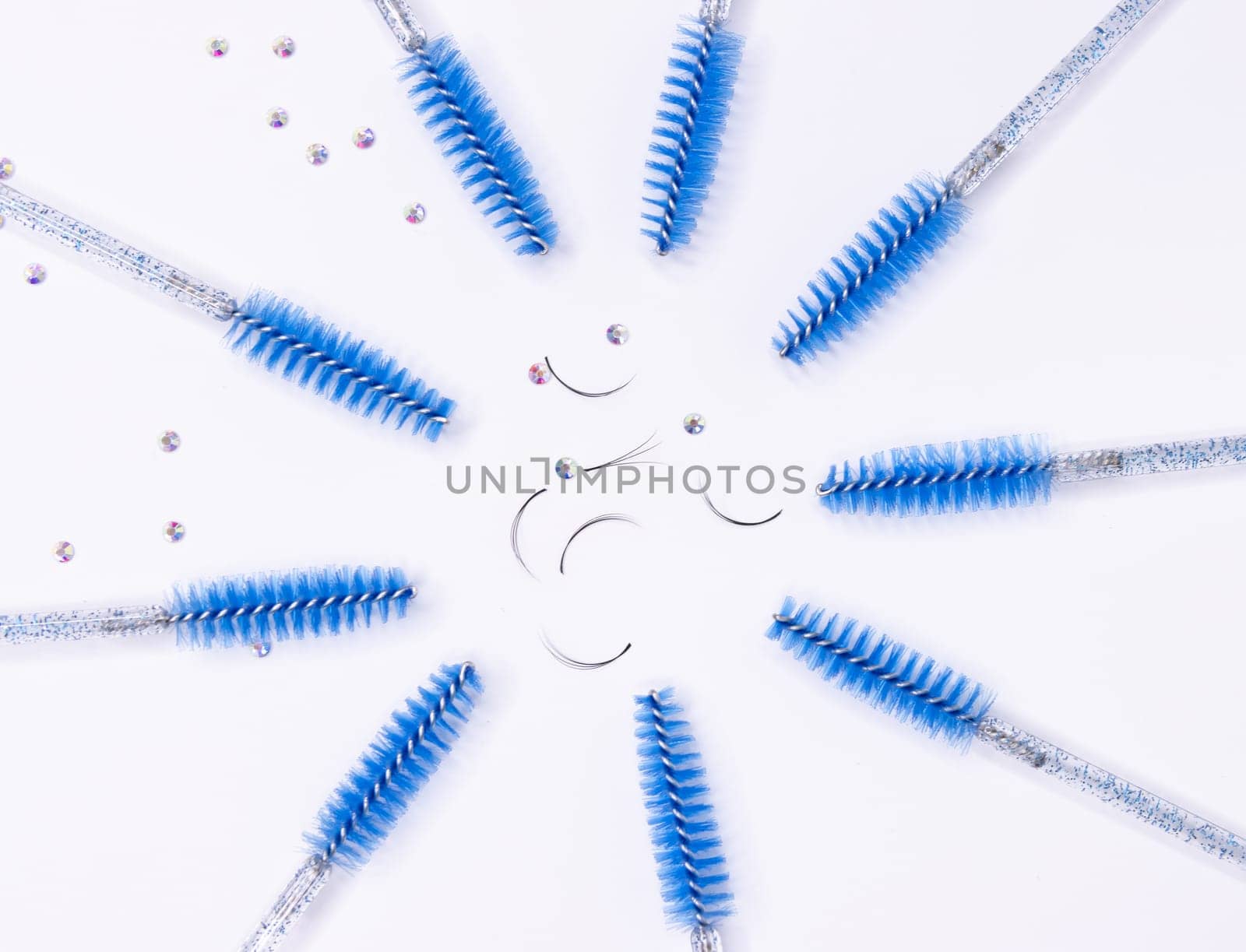 Accessories for eyelash extensions.Blue brushes, pebbles and eyelashes.A circle is laid out with blue eyelash brushes on a white background,pebbles and artificial eyelashes are all over the background