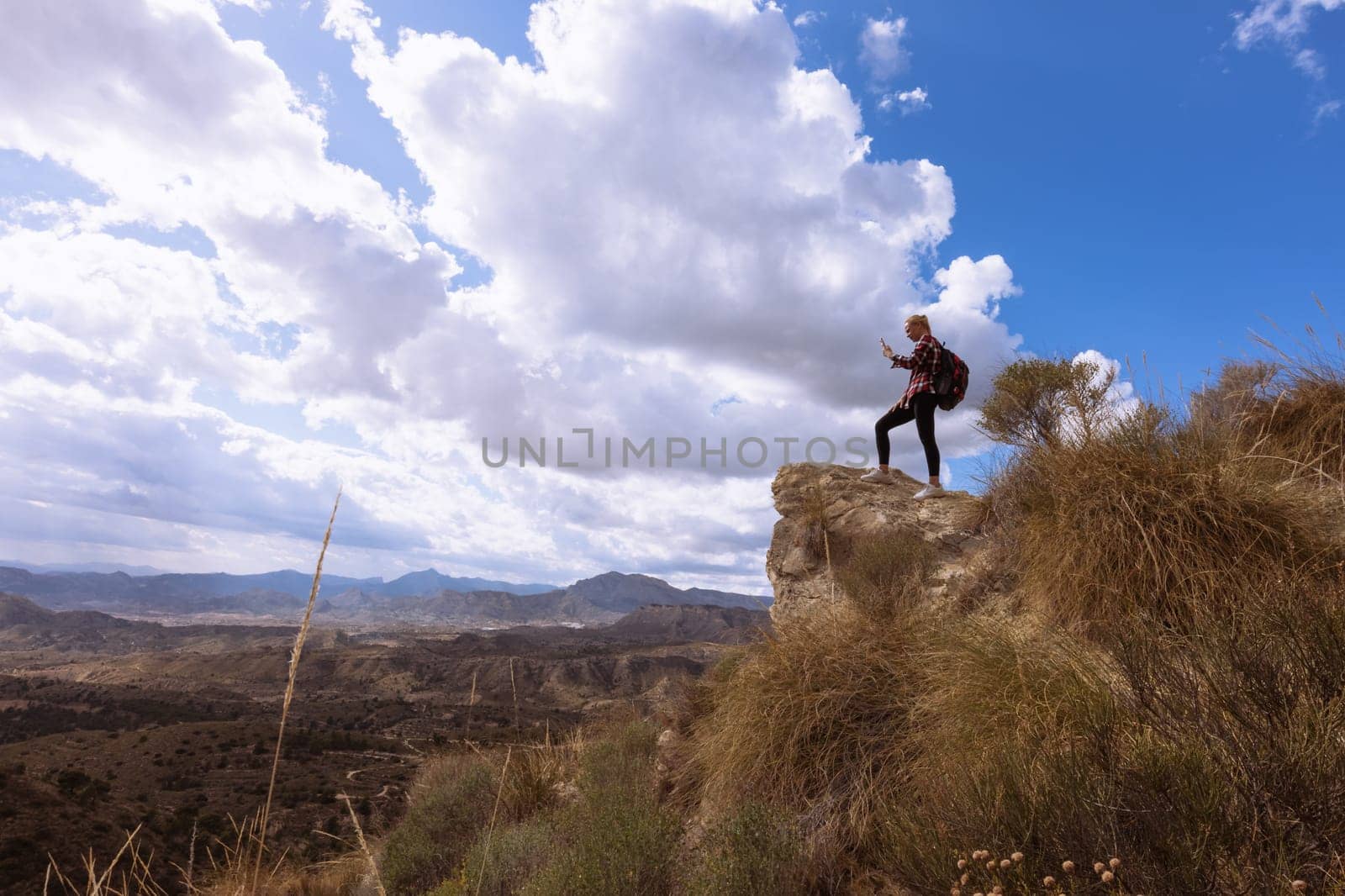 a girl in sportswear stands at a height and looks at a beautiful view of the mountains, a beautiful landscape of nature by PopOff