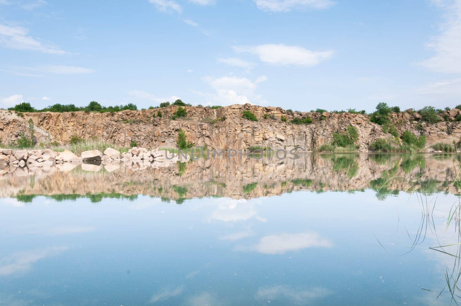 Photo of nature in the park, a lake with blue water and mountains with stones with green grass, a beautiful blue sky. Picturesque nature without people