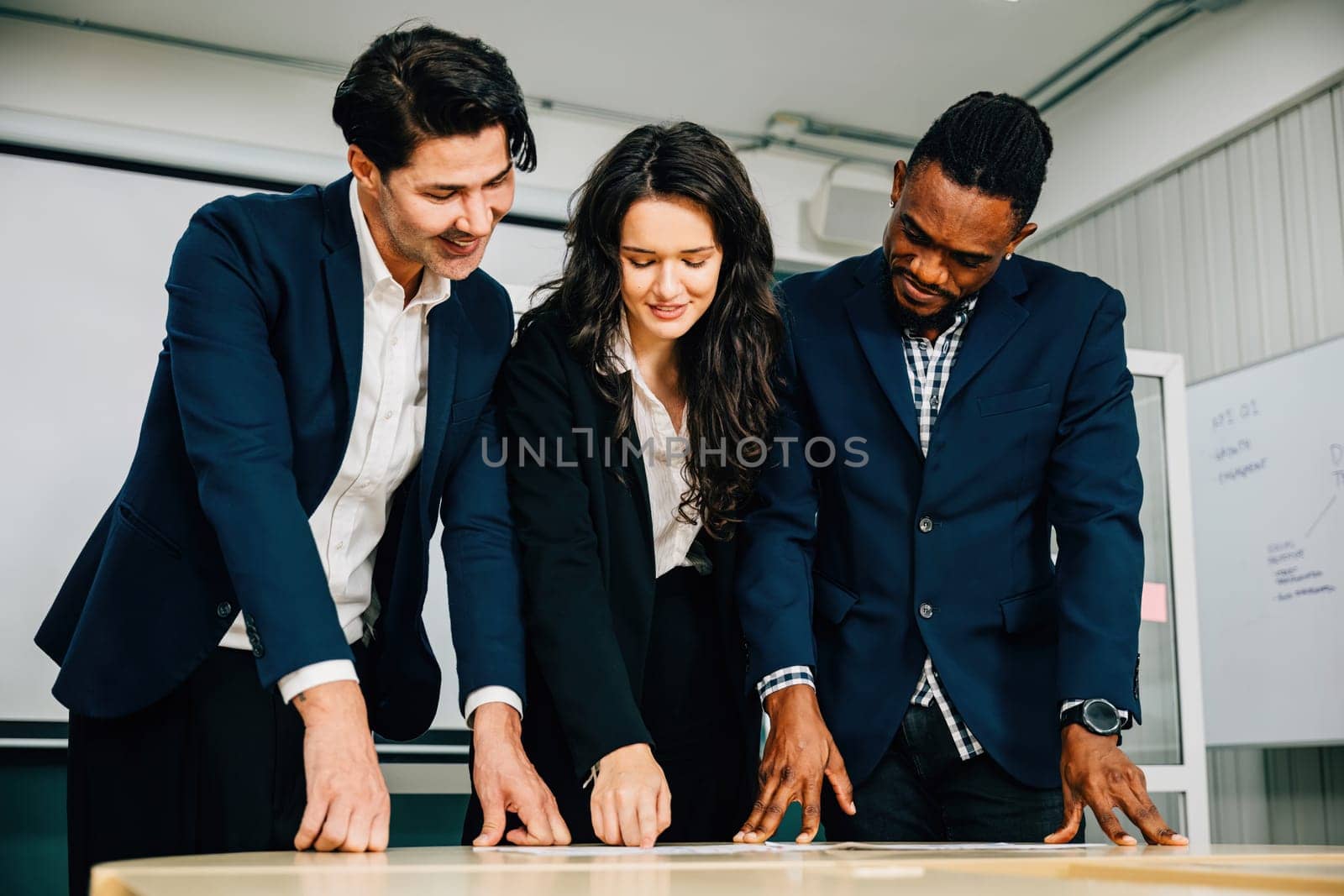 In an office conference room, businesspeople stand and discuss for a successful meeting. Teamwork, diversity, and effective communication are essential. by Sorapop