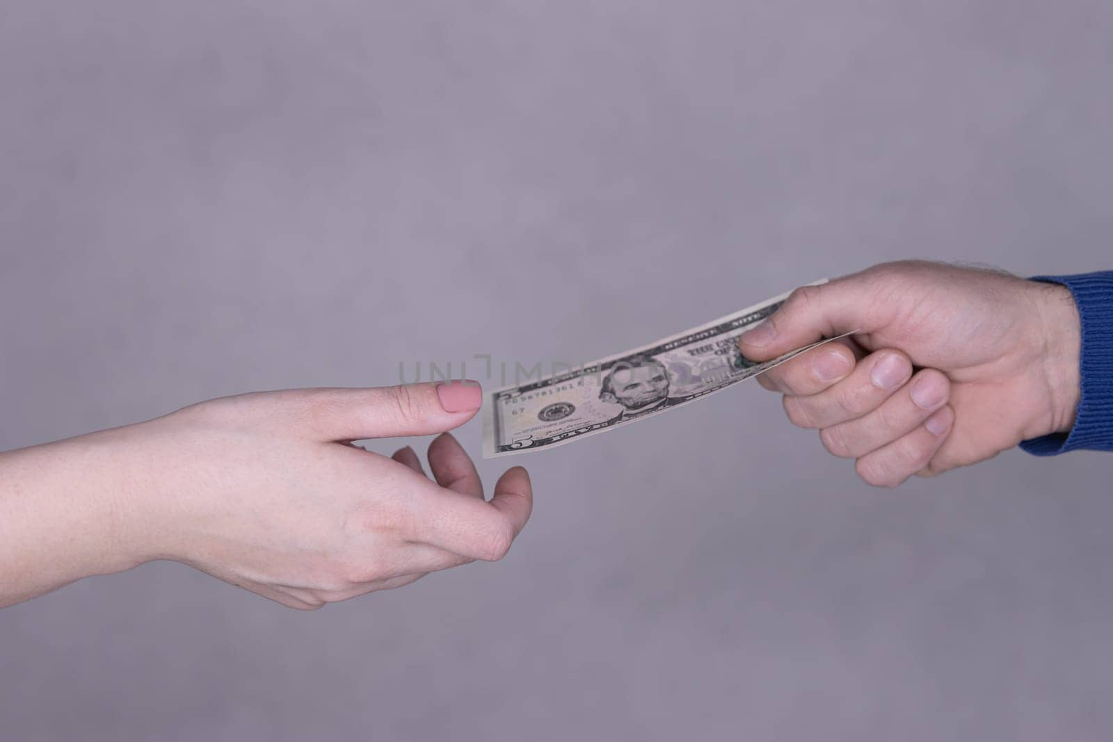 hands giving money 5 dollars isolated on gray background close-up.Finance concept.male hand in a blue sweater gives dollars to female hands on a gray background. High quality photo