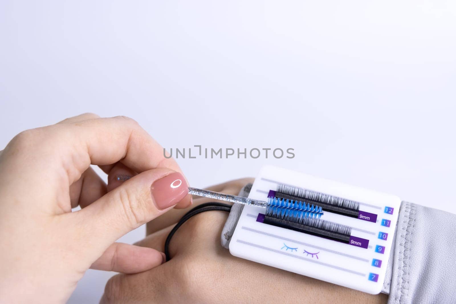 a female hand combs artificial eyelashes with a blue brush, black eyelashes are glued to a white palette