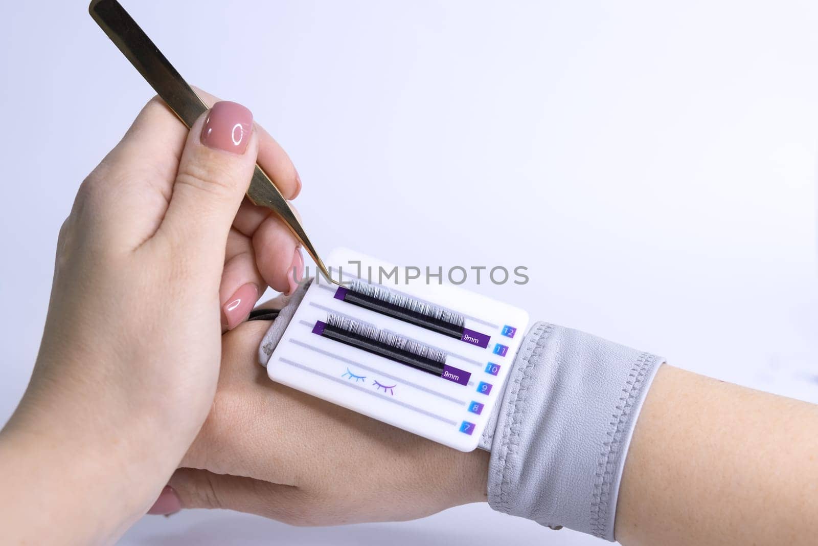 female hand holds eyelash extension tweezers and takes eyelashes, black eyelashes are glued on a white palette High quality photo