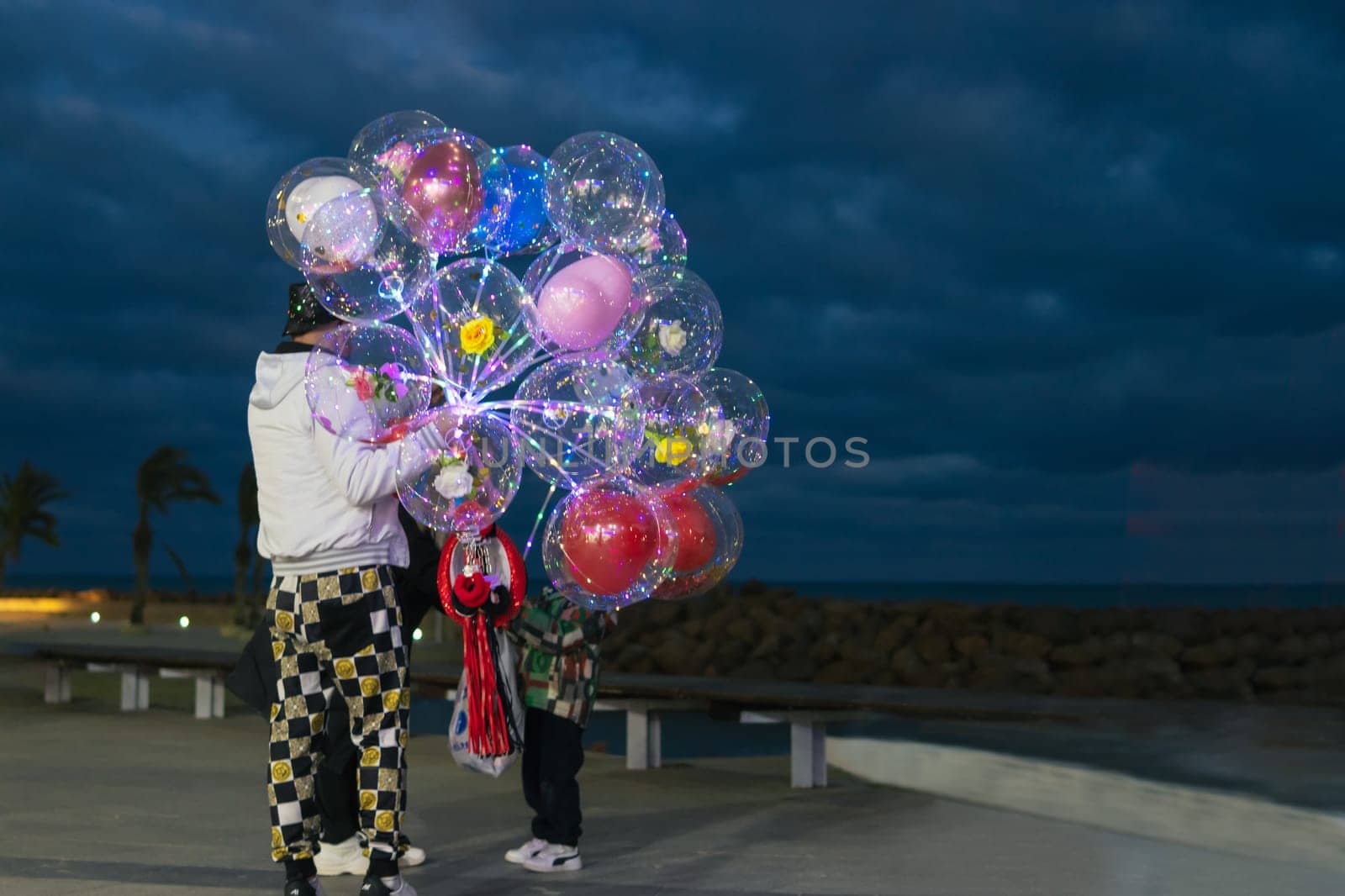 a guy on the embankment sells beautiful balloons in the evening, a man stands with his back to the cameras and holds a lot of balloons in his hands there is a place for an inscription by PopOff