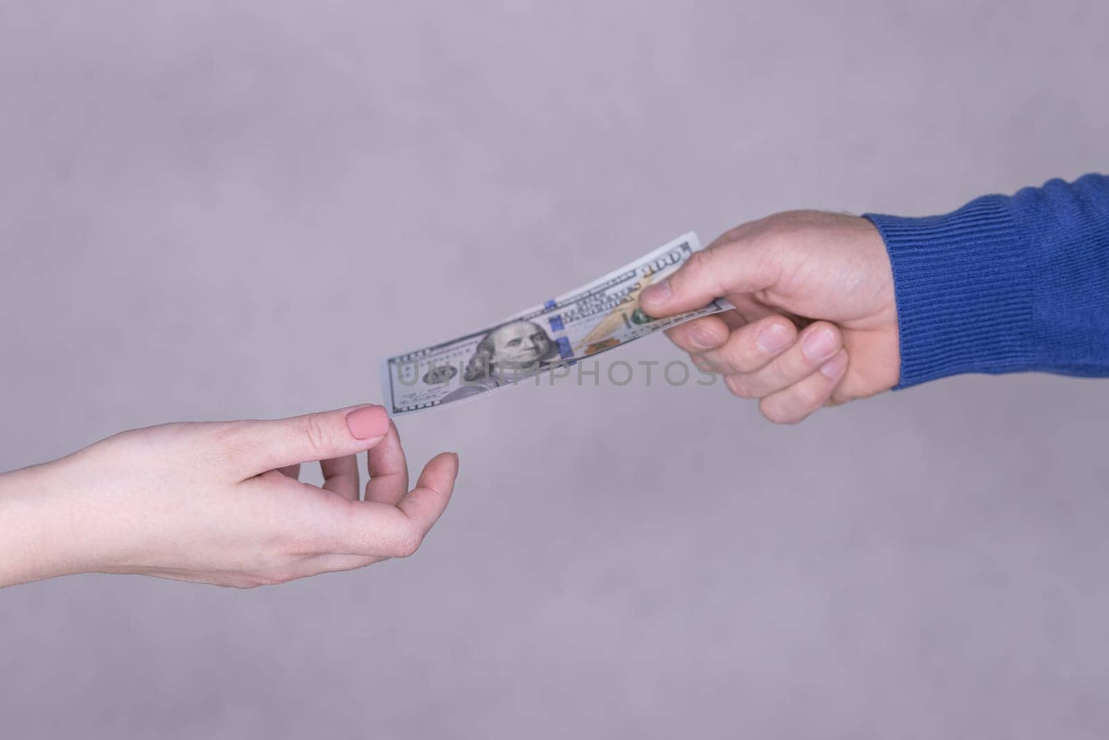 hands giving money 100 dollars isolated on gray background.Finance concept.male hand in a blue sweater gives 100 dollars to female hands on a gray background. High quality photo