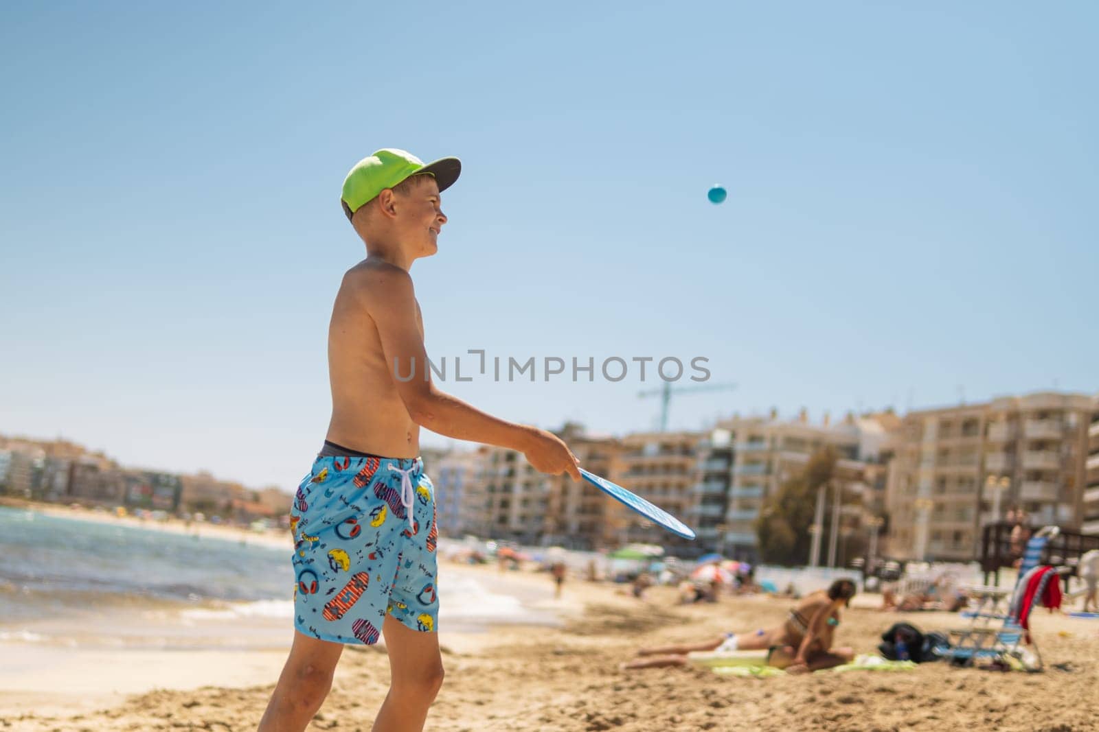 happy child of European appearance on the beach walks in tennis, the boy is standing in swimming trunks and in a green cap on the beach, a happy child is resting on the sea. High quality photo