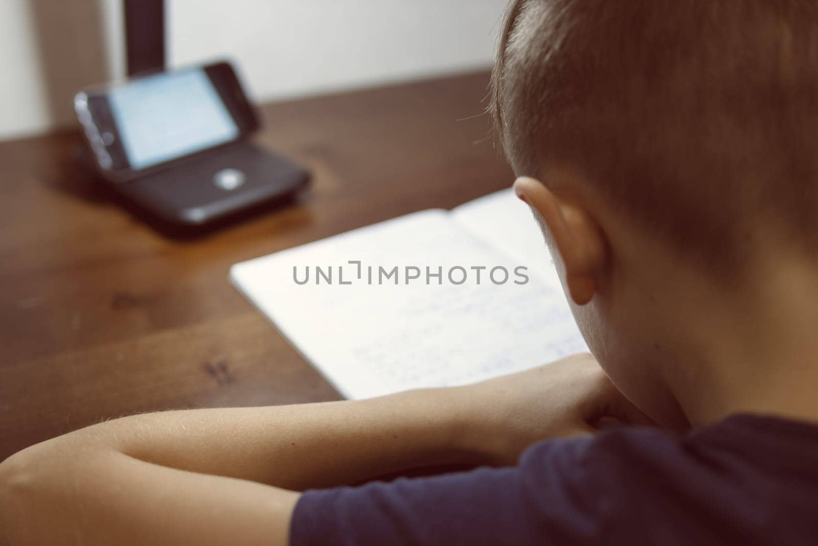 boy doing homework in children room on distance learning in front by PopOff