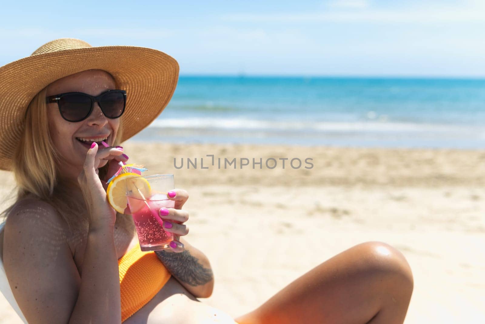 Happy young european girl drinks a cocktail and rests in a sun lounger on the beach, space for an inscription . High quality photo
