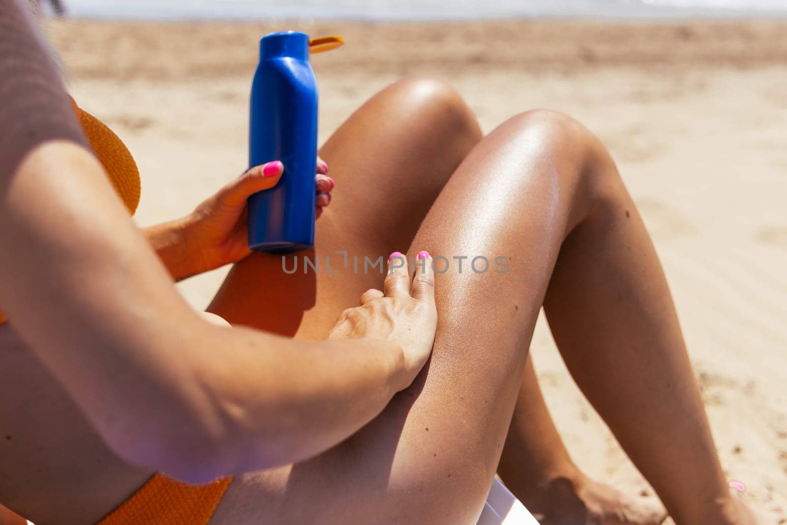 the girl is holding a blue bottle of sunblock cream in her hands on the beach, the girl is sitting on a sun lounger in a swimsuit. High quality photo