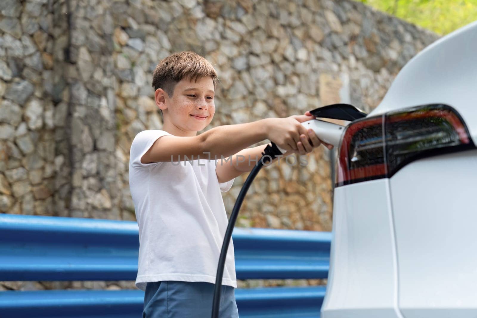 Little boy recharging eco-friendly electric car from EV charging station. EV car road trip travel concept for alternative transportation powered by clean renewable and sustainable energy. Perpetual