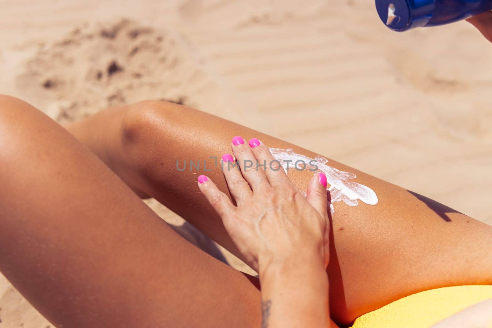 Sunscreen for skin care. Close-up of woman's legs applying sun lotion before sunbathing. Beautiful dark-skinned woman applies cream on her tanned leg . high quality photo. High quality photo