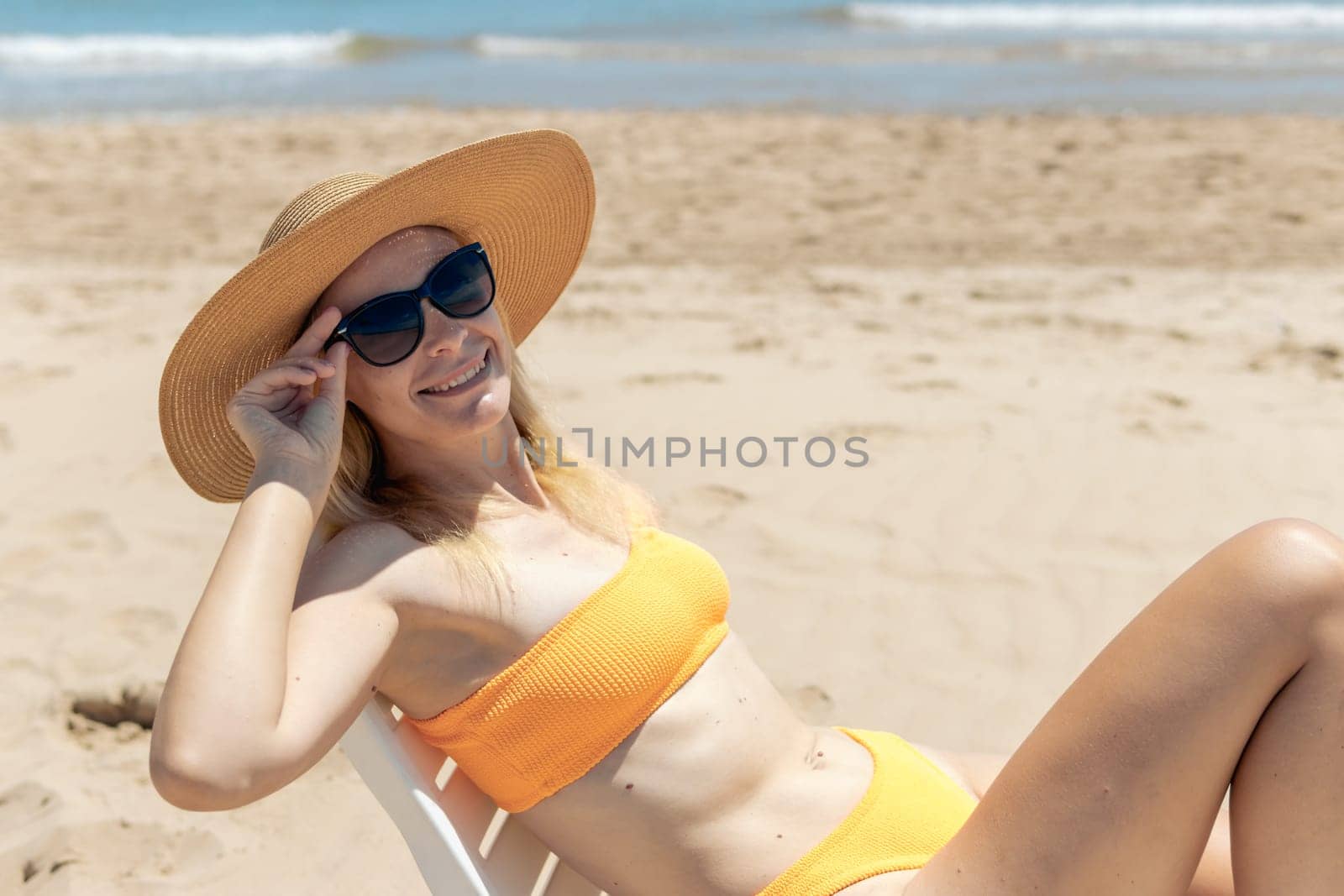 Portrait of a happy european woman in an orange swimsuit sunbathing on a plastic sun lounger on a tropical beach, looking at the camera. High quality photo